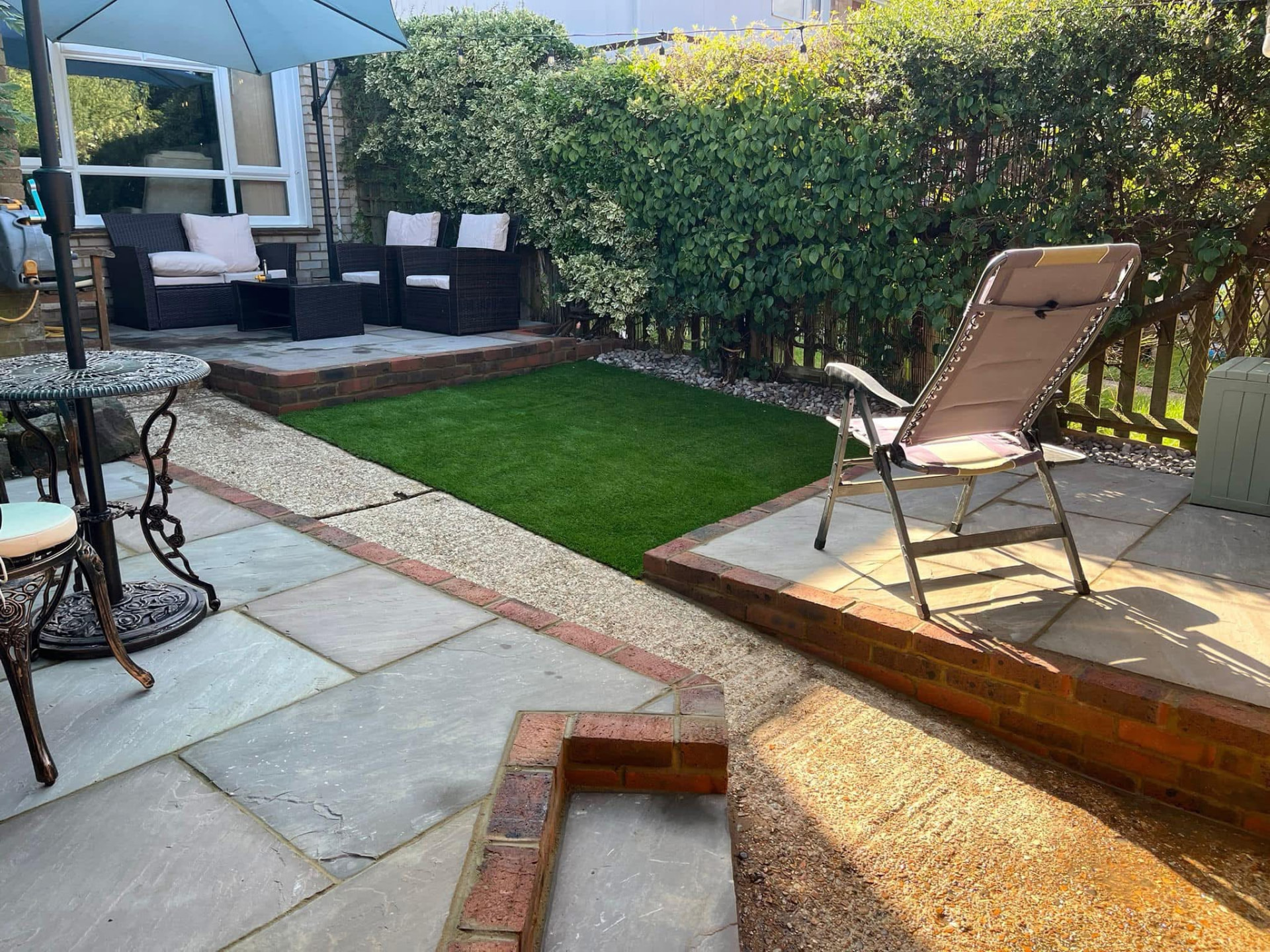 Split-level Indian sandstone patios with brick edge details, artificial lawn and garden seating