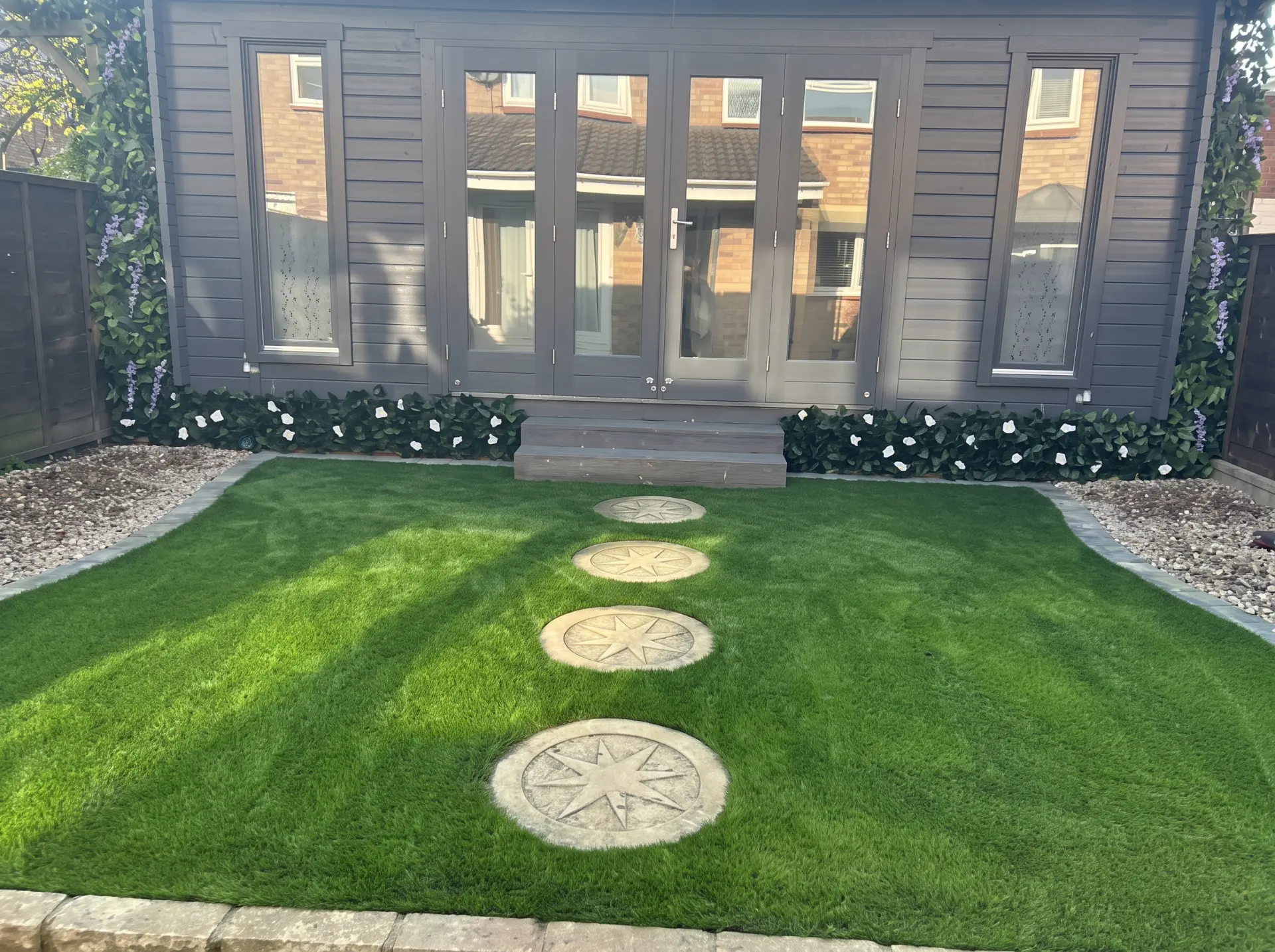 Garden room with grey cladding and glass doors, artificial lawn, gravel borders and decorative stepping stones
