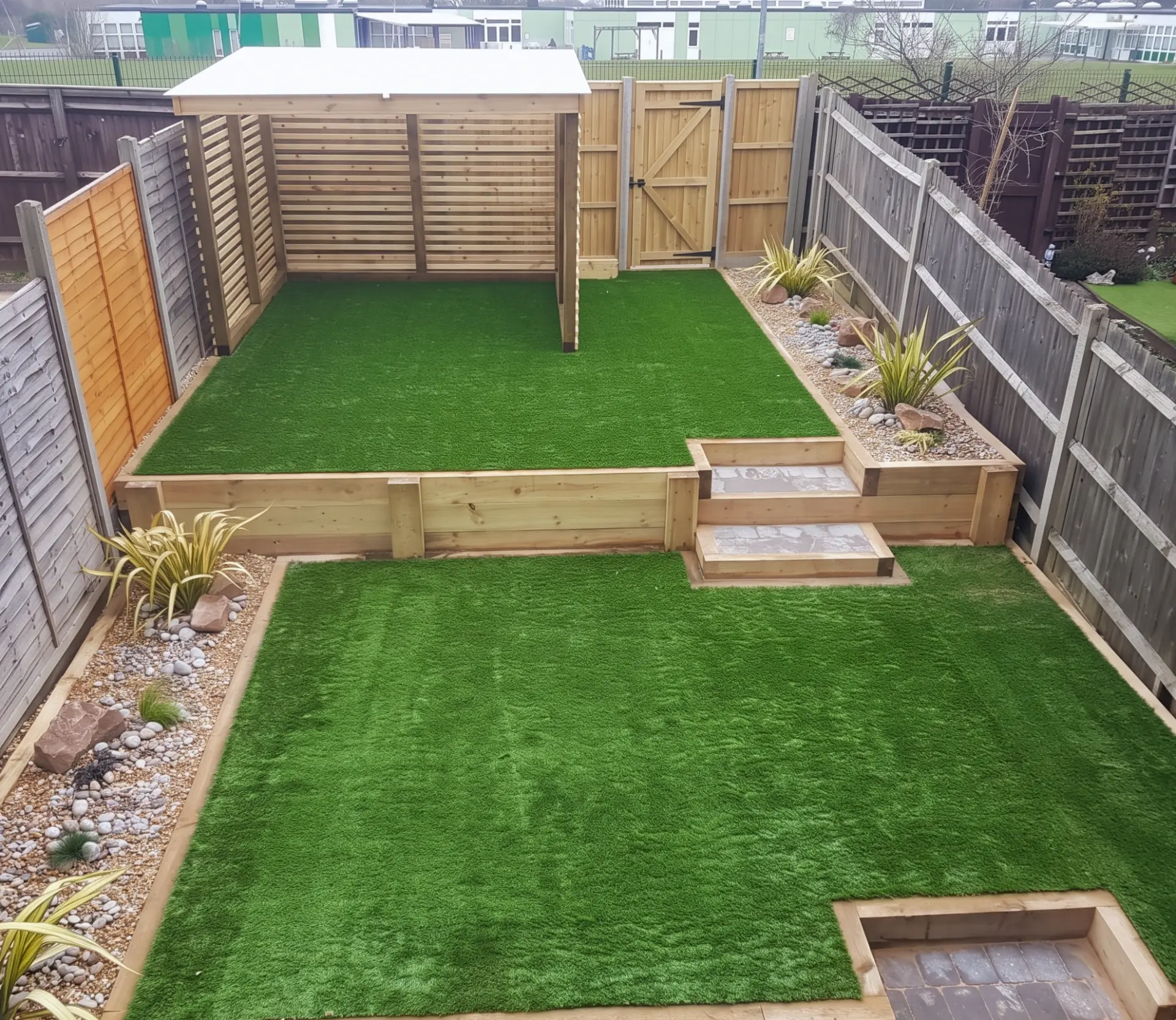 Split-level garden with artificial lawns, timber sleeper steps and raised beds, gravel borders and a timber shade screen